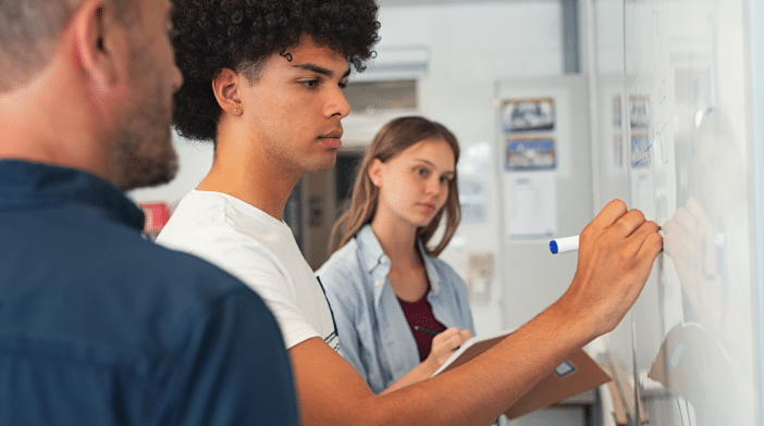 Students work through a maths problem while a teacher watches