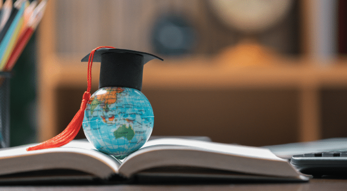 Globe with a graduation cap resting on the seam of an open book